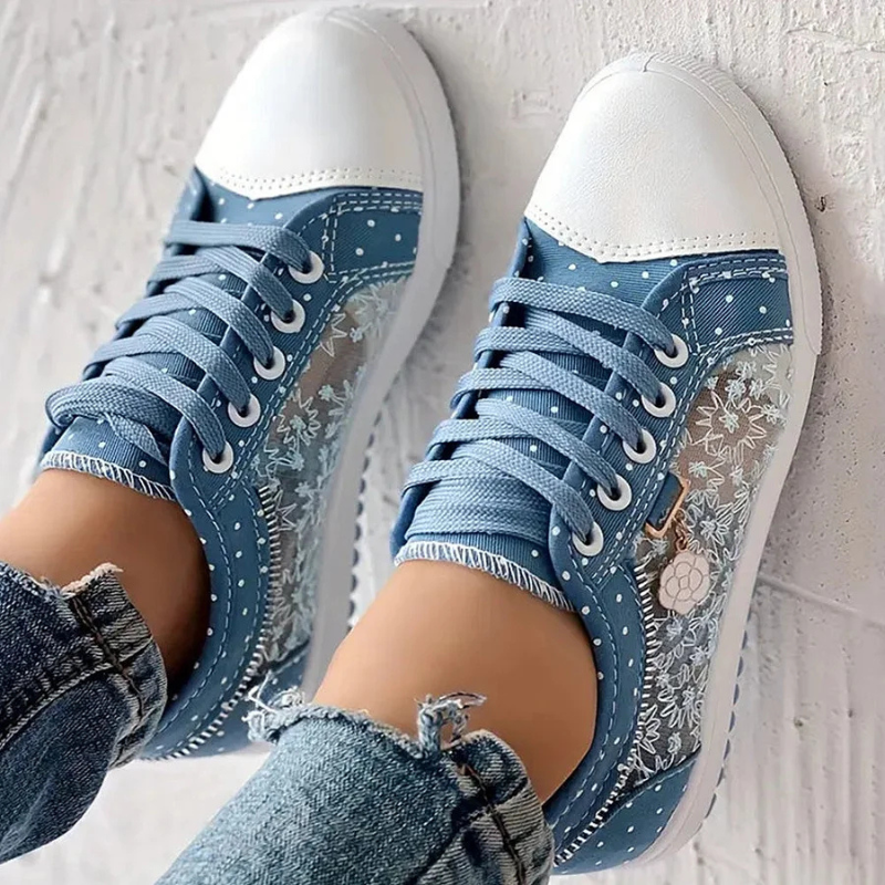Damskie obuwie casual: niebieskie sneakersy z eleganckim haftem kwiatowym i ozdobną zawieszką.