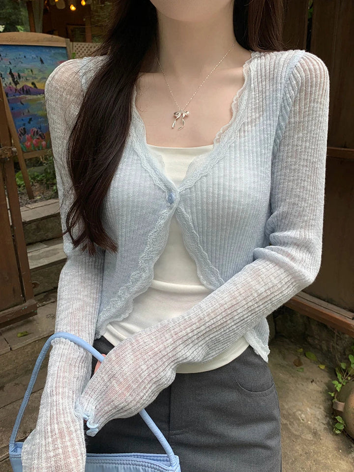 Krótki top typu crop top, damski, z delikatną koronką i ozdobnym guzikiem. Długi rękaw.